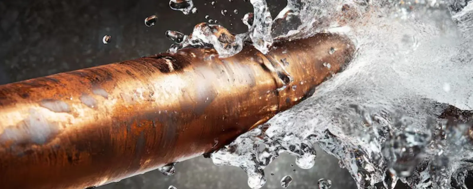Copper pipe split open and spraying water against a dark background
