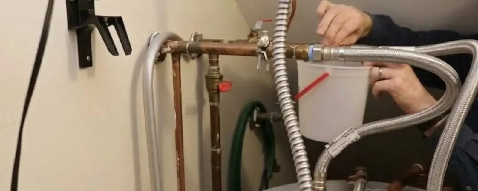 Hands connecting braided flexible supply lines and copper pipe at the top of a water heater