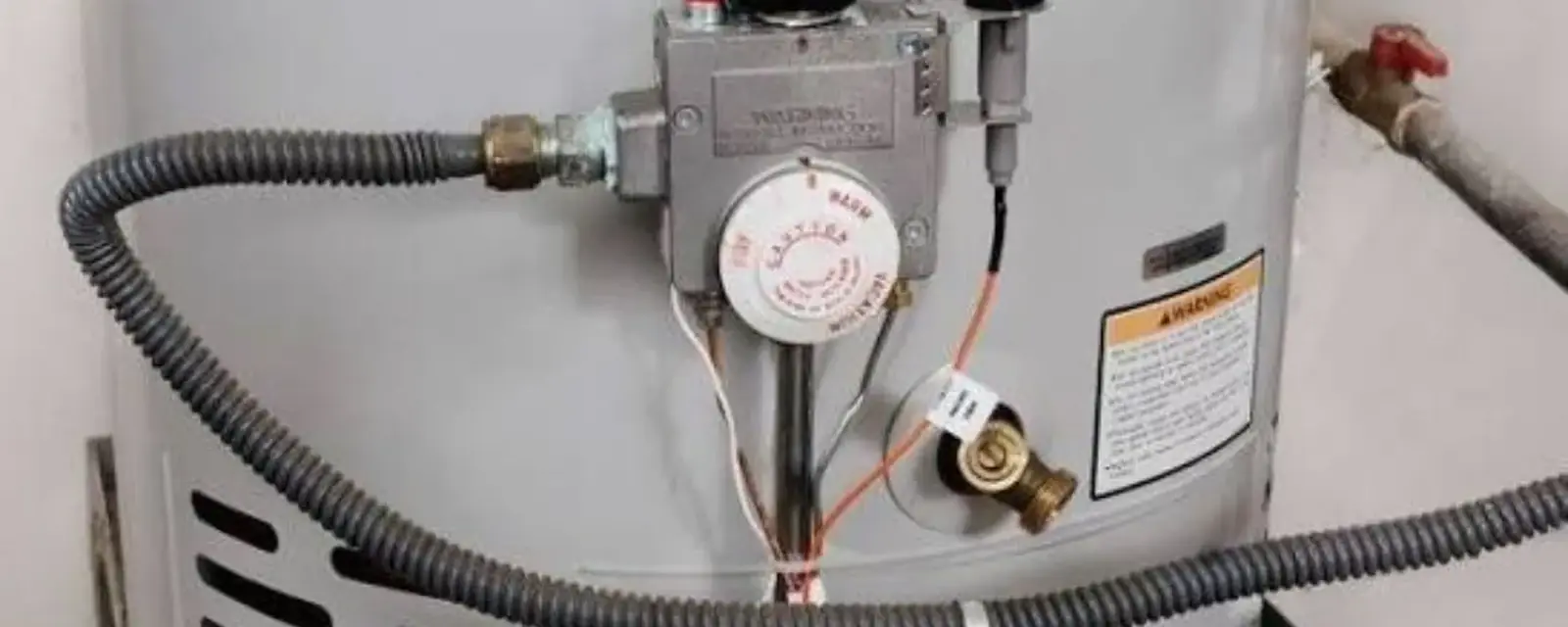 Gas control valve, thermostat and flexible gas line on the side of a white tank water heater